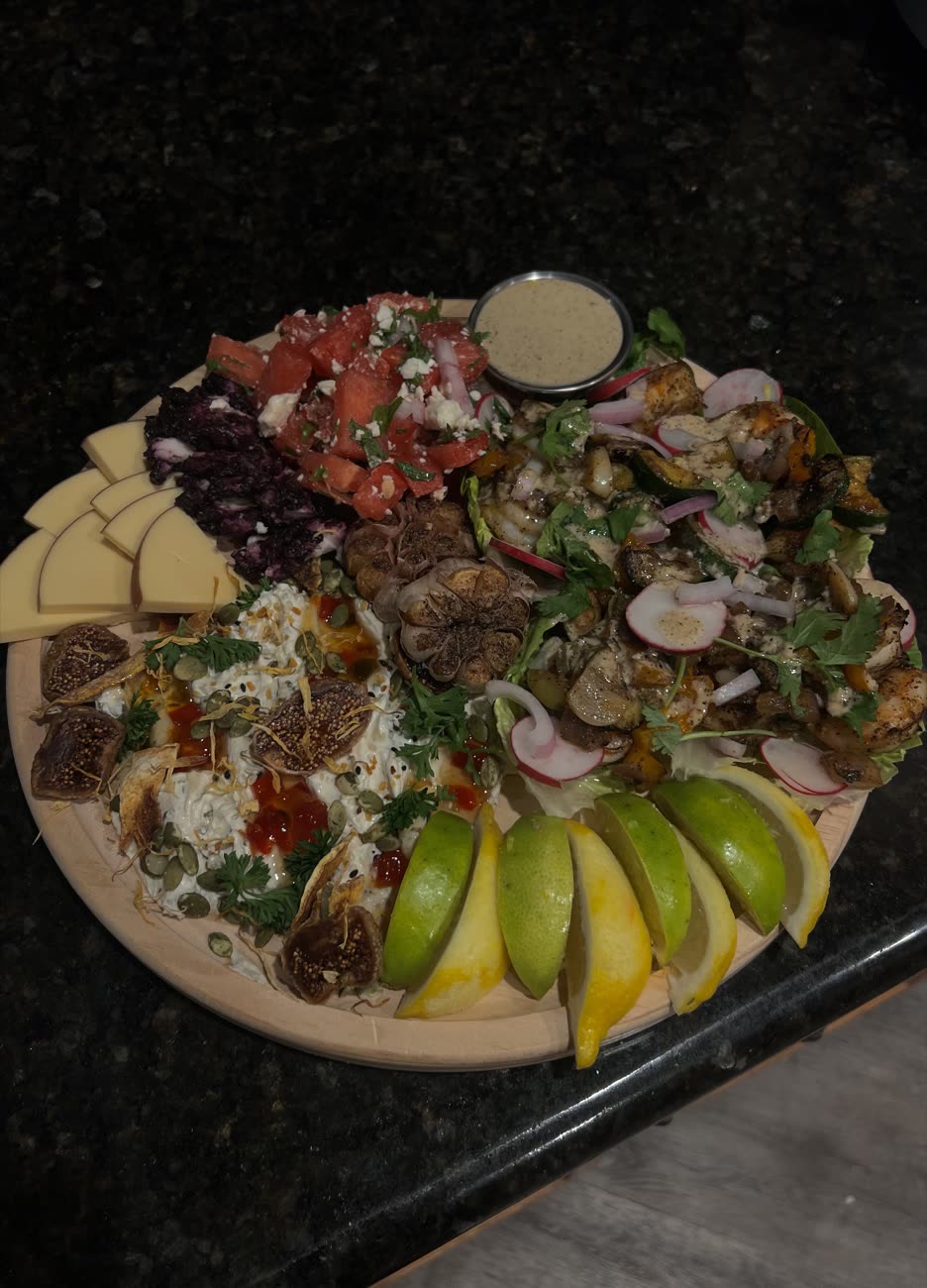 A grazing board built by Destiny: watermelon and feta, labneh with chili crisp and dried figs, roasted garlic, grilled chicken salad, cheeses, and sliced apples