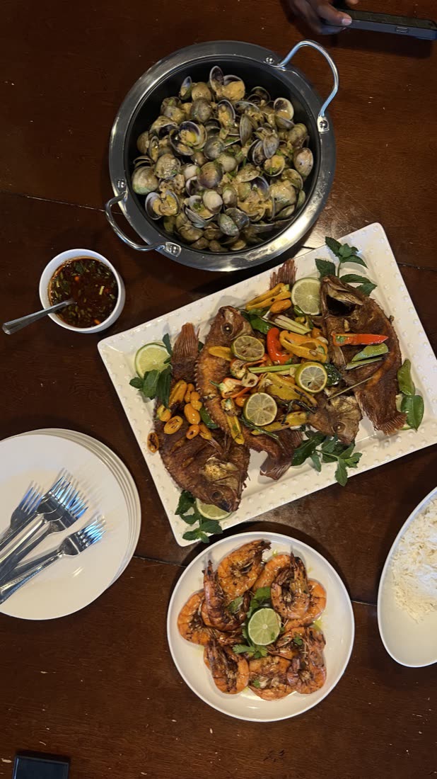 A family-style seafood spread: steamed clams, whole fried fish with citrus and peppers, grilled shrimp with lime