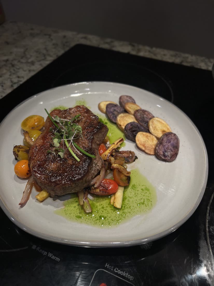 Plated steak over blistered tomatoes and herb oil with fingerling and purple potato coins